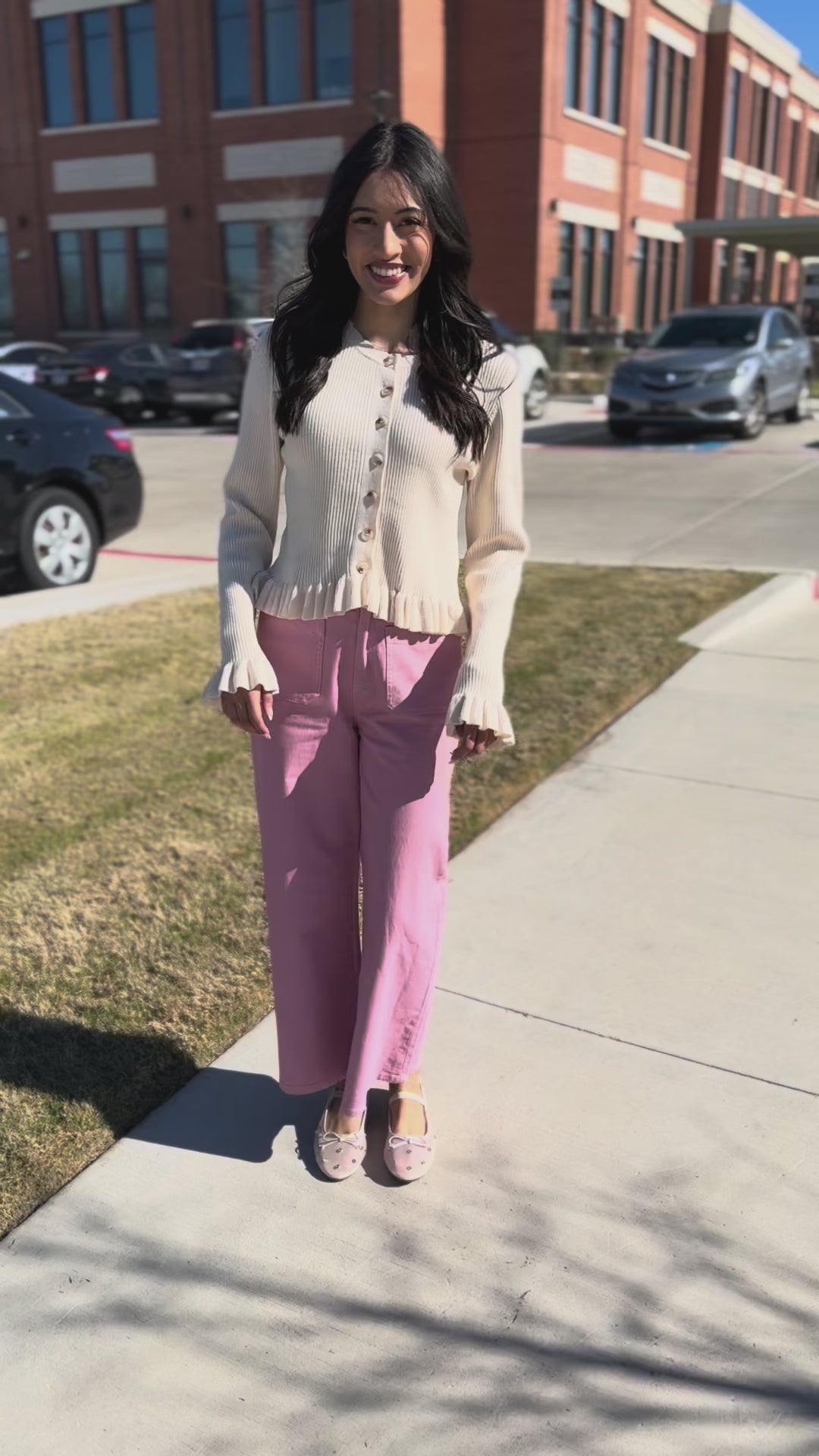 Woman wearing a cream cardigan and pink pants on a city street.