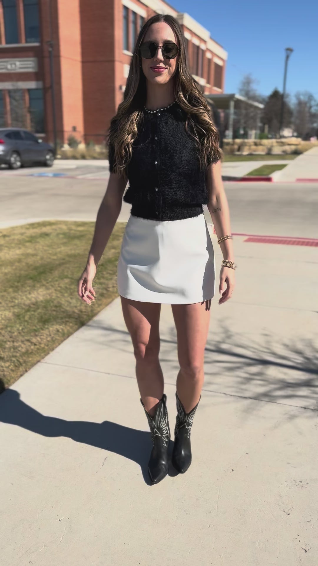 Woman wearing a black top and white skirt with sunglasses outdoors.