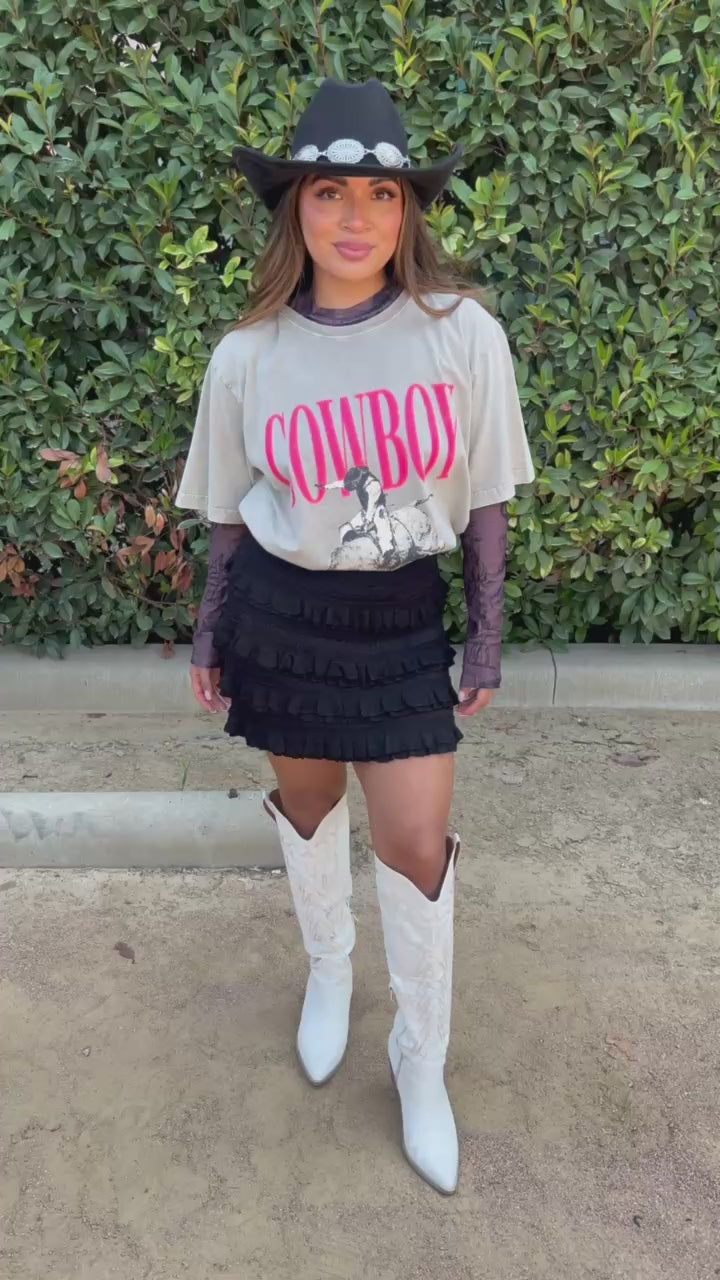 Brunette model in a graphic tee, mesh, and black skirt in an outdoor setting. Southern House Clothing