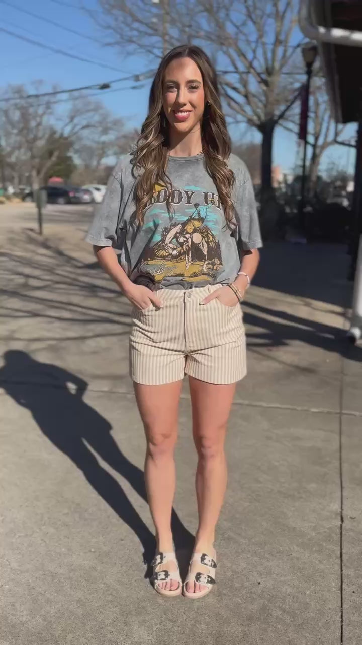 Woman wearing a gray graphic t-shirt with text and graphics, standing outside.