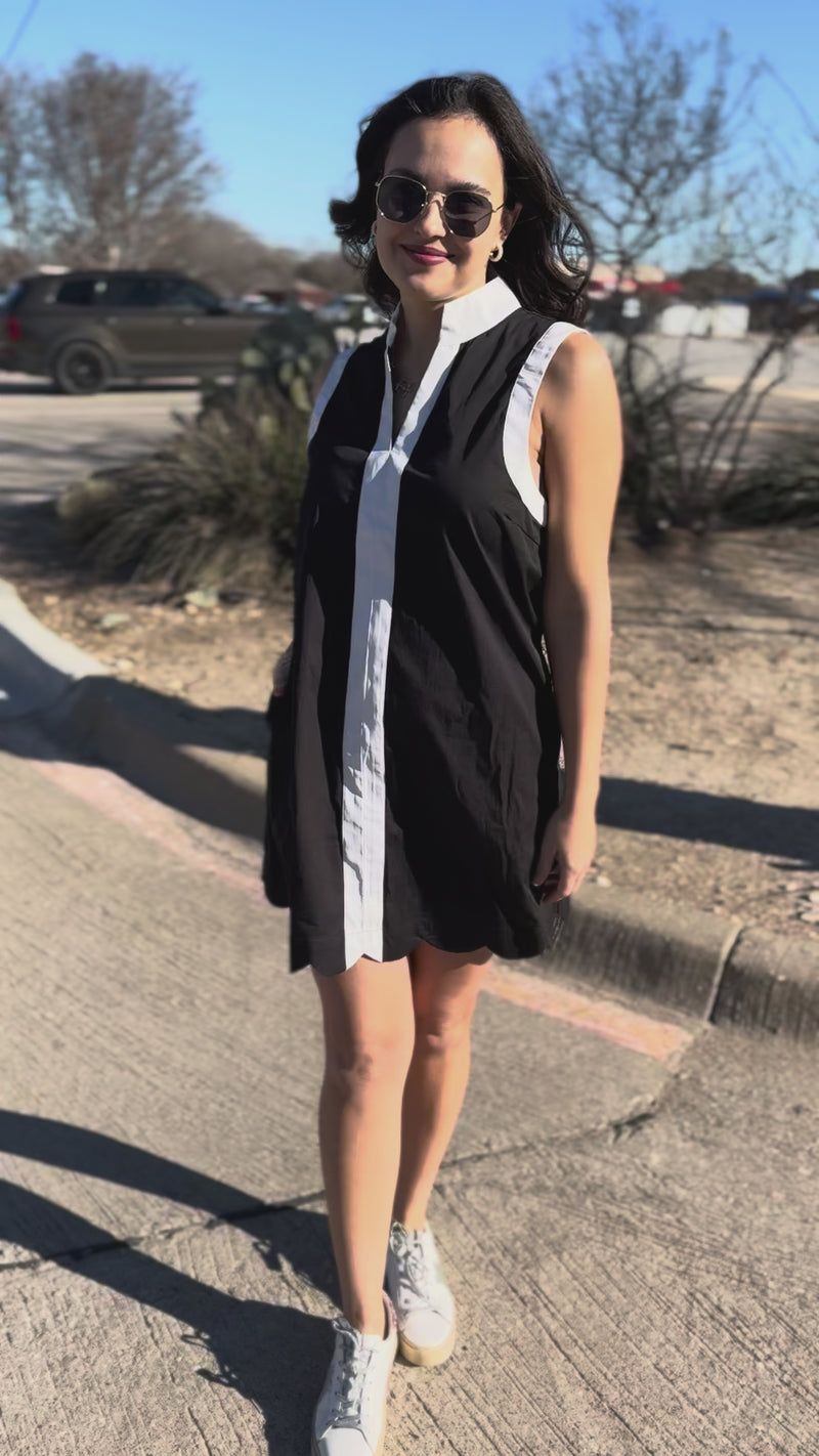 Woman wearing a black and white dress with sunglasses standing outside.