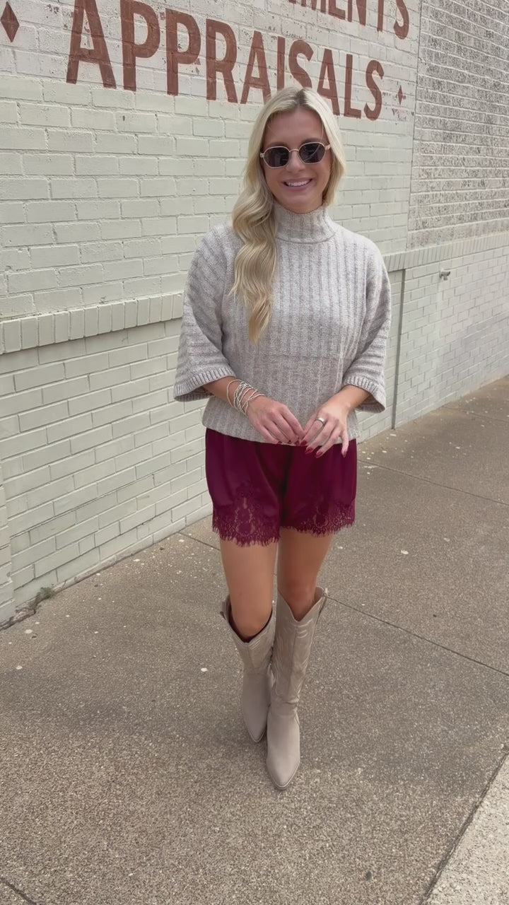 Blonde model wearing an oatmeal color sweater top and burgundy laced trimmed shorts outside. Southern House Clothing