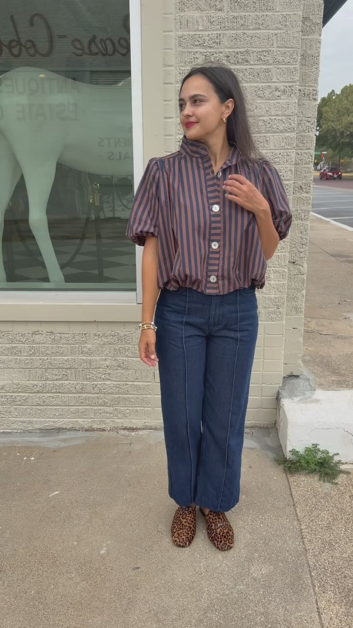Brunette model wearing a navy and brown stripped bubble top and dark denim jeans outside. Southern House Clothing