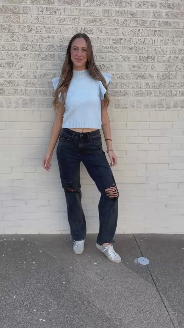 Blonde model wearing a lightweight blue sweater top and black jeans outdoors.