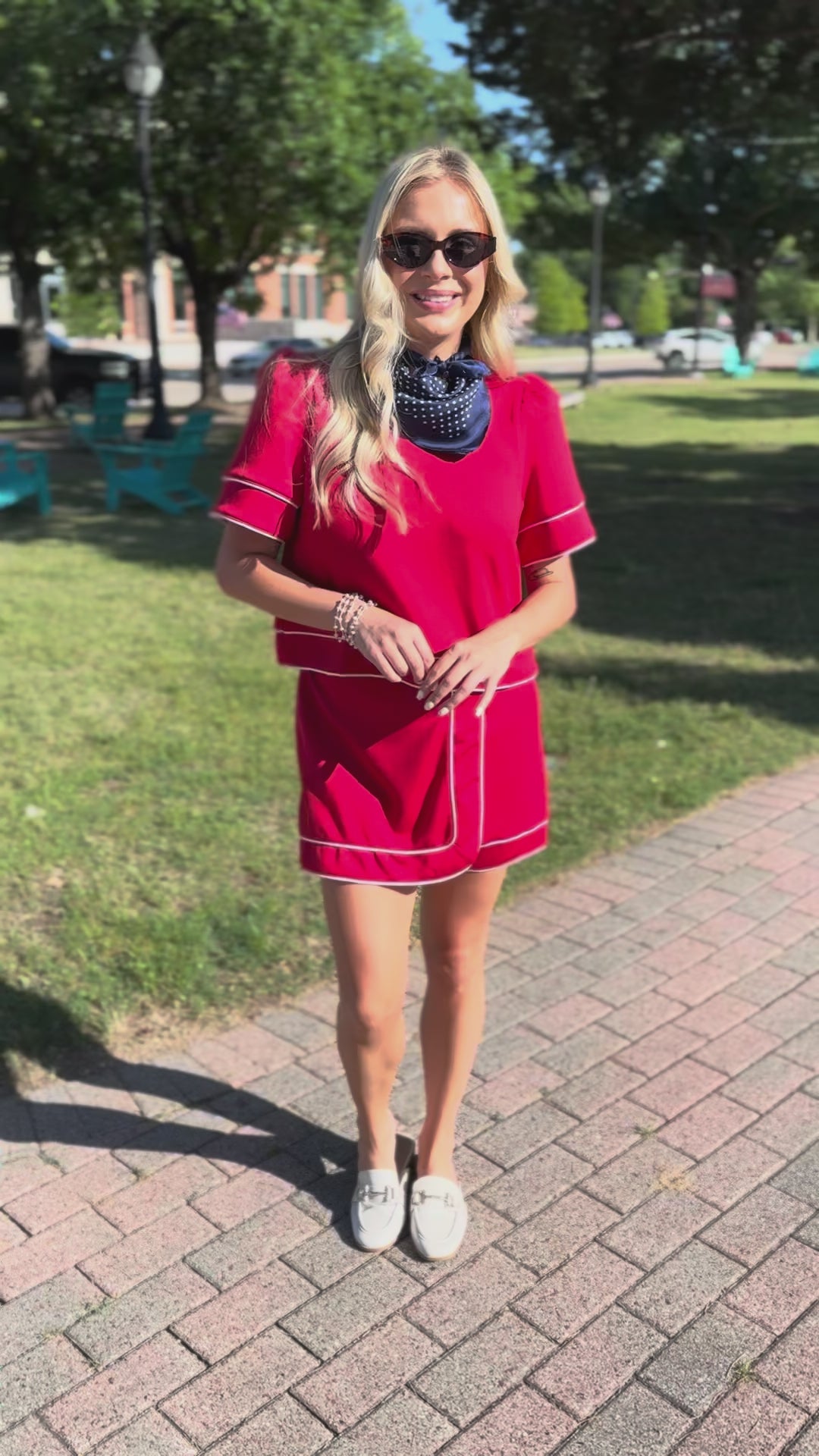 Woman in a red dress standing on a sidewalk with a park in the background