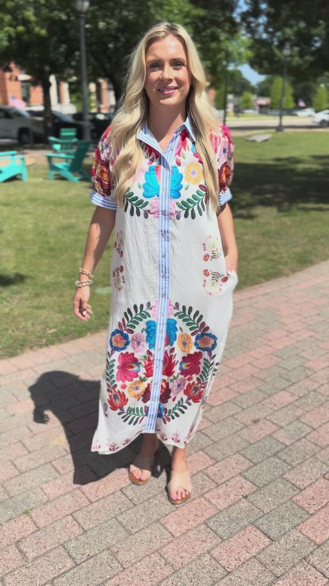 Blonde model is a ivory multi-colored dress standing outside.