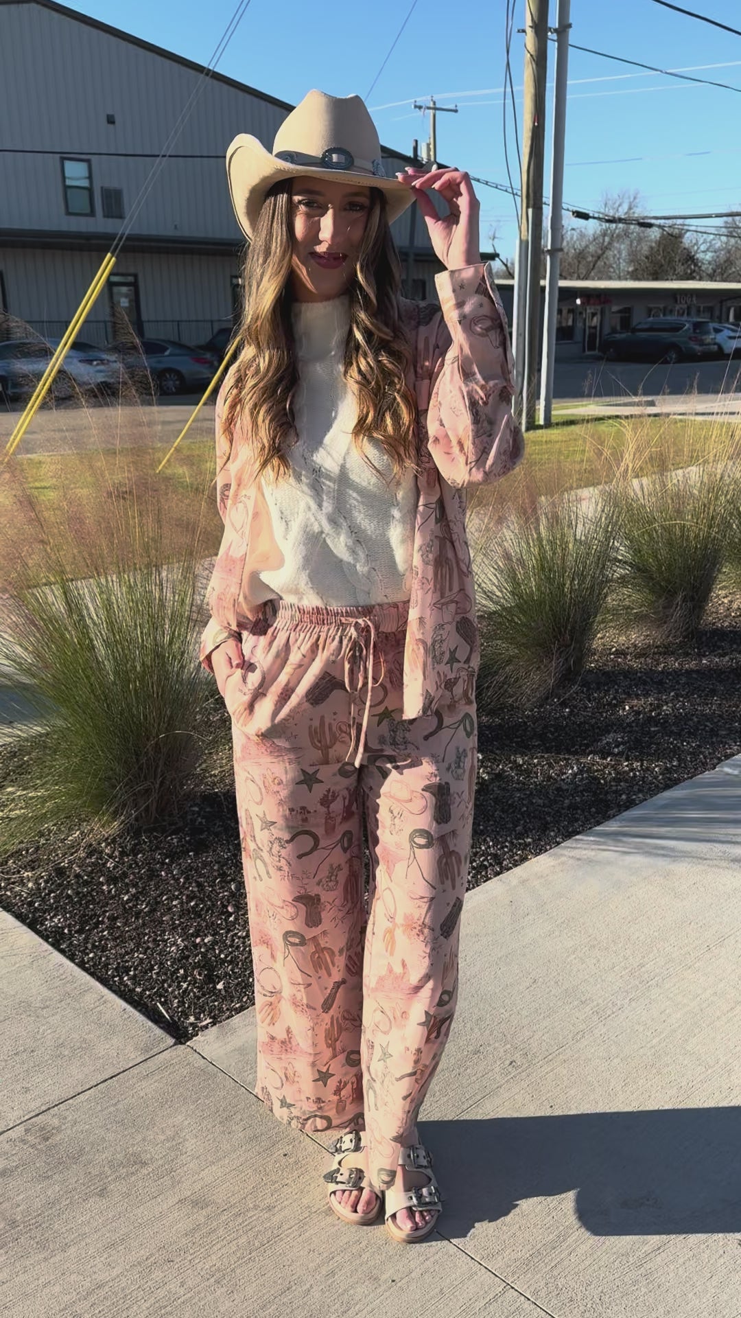 Woman wearing a white sleeveless top and patterned pants with a beige cowboy hat.