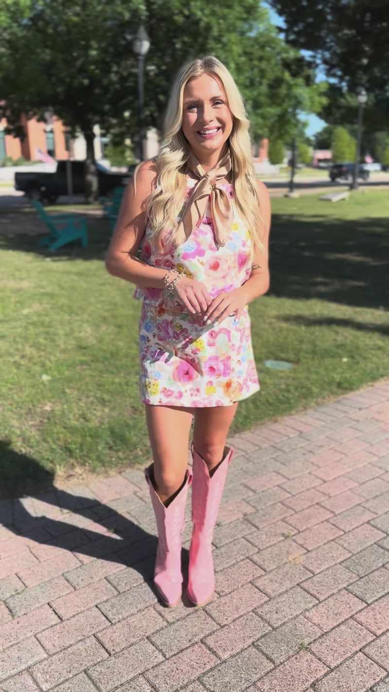 Woman wearing a floral set and pink cowboy boots standing outside.