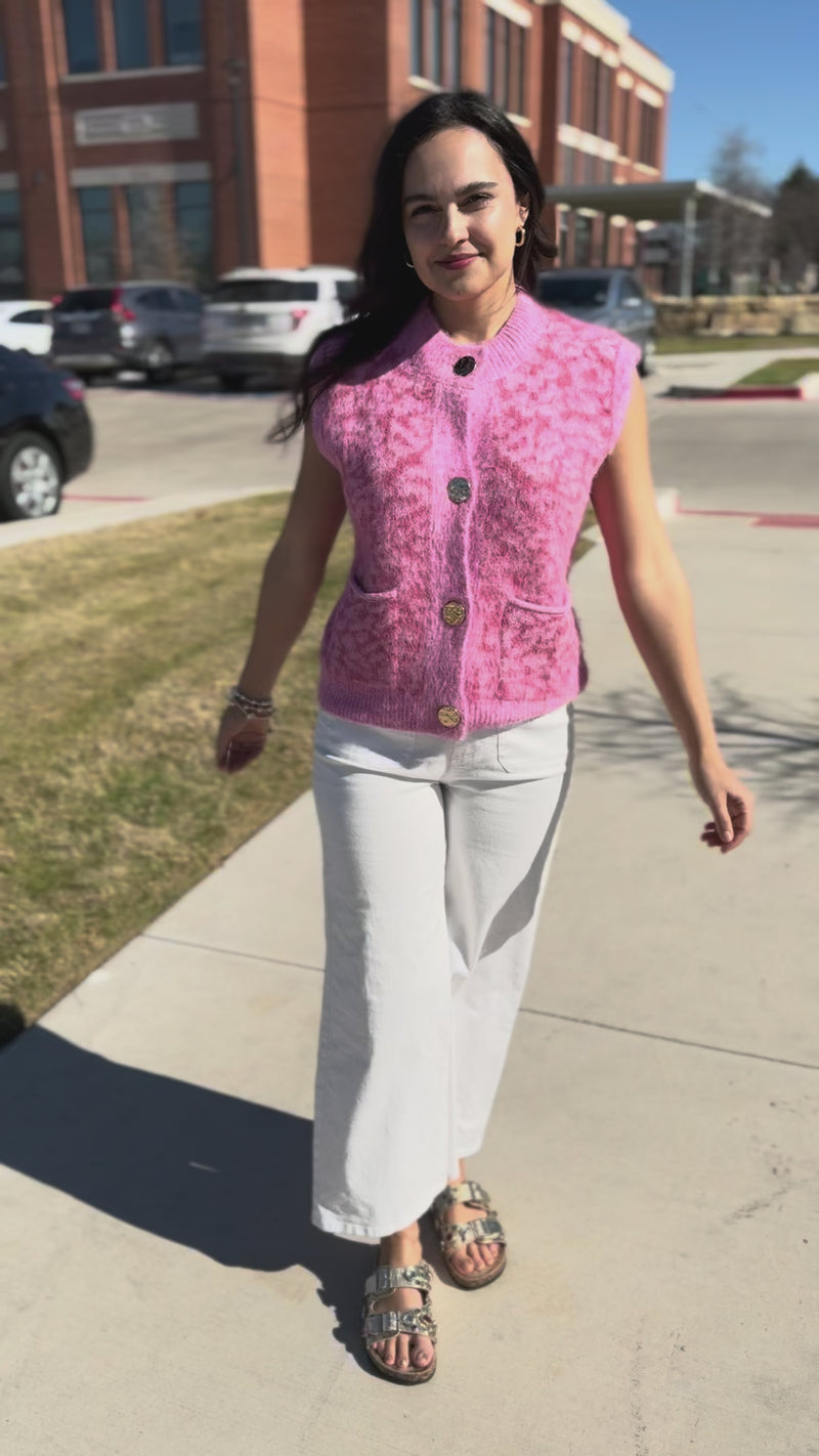 Woman wearing a pink vest with gold buttons and white pants outdoors