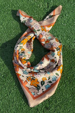 Taupe scarf with flower design laying on green turf backdrop.