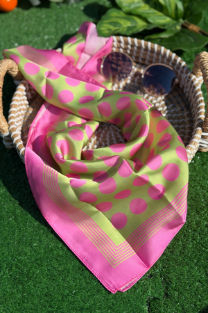 Pink and green polka dot scarf on a grassy surface with wicker baskets in the background.