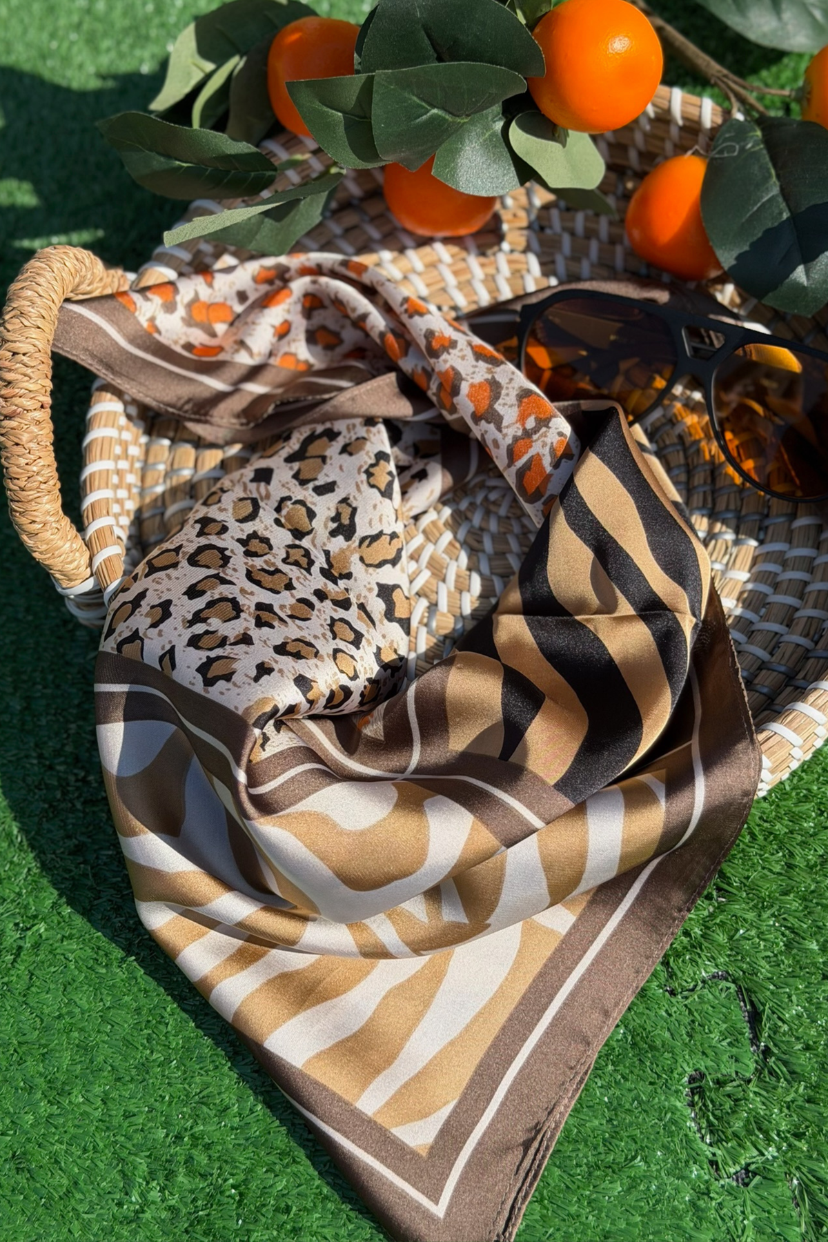 Patterned scarf draped over a woven basket with oranges and leaves on a green background