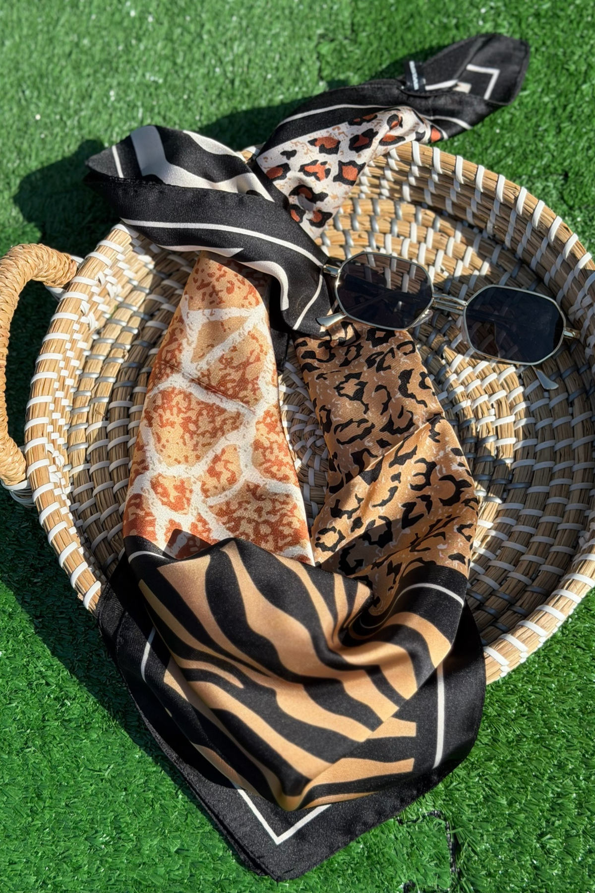 Woven basket with patterned scarves and sunglasses on a green grass background