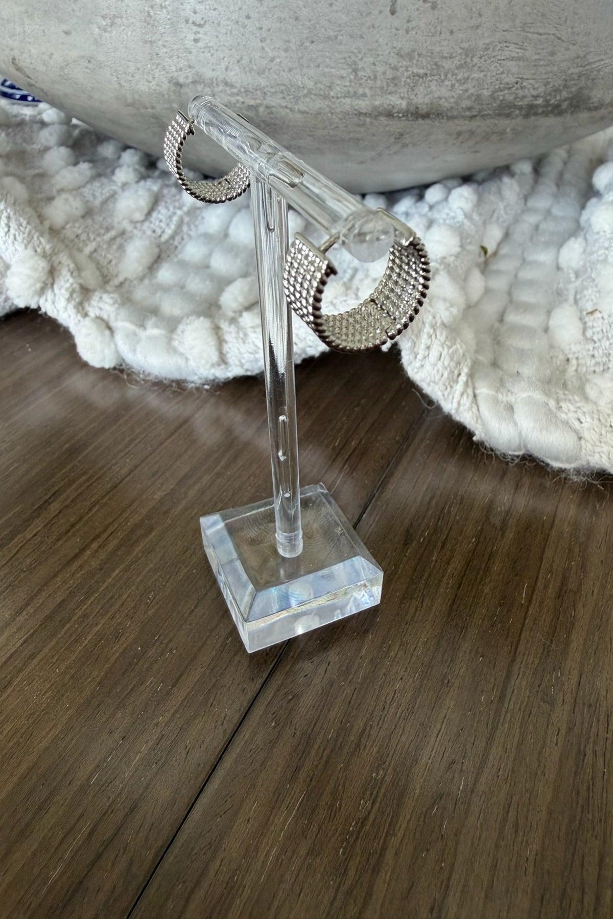 Pair of silver hoop earrings on a clear stand with a textured white surface in the background.