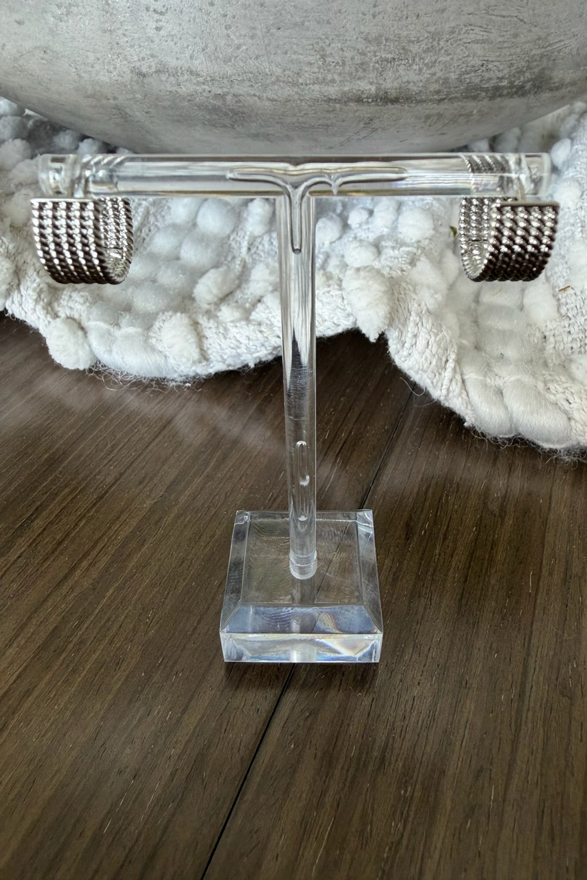 Clear acrylic T-shaped stand on a wooden surface with a textured white object in the background.