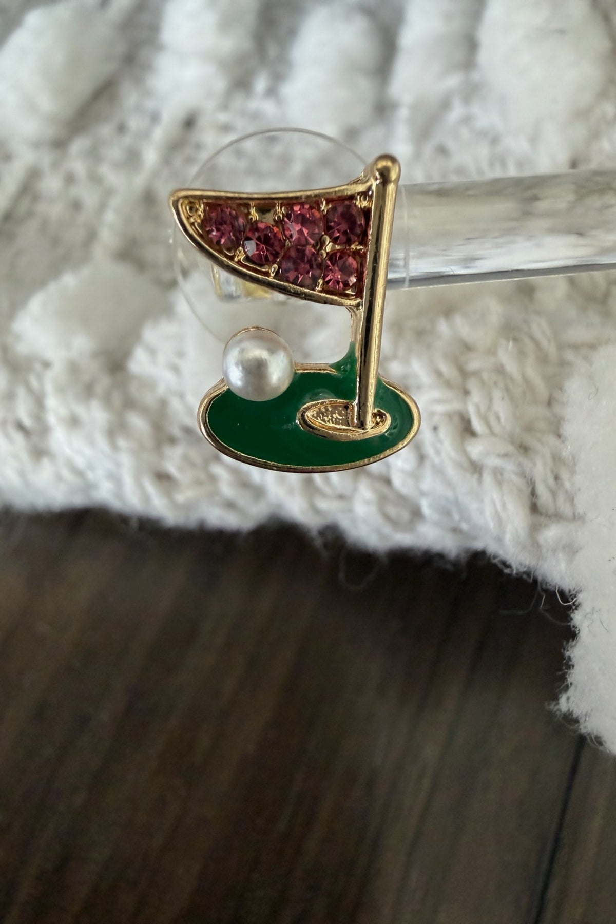 Decorative brooch with green base, gold flag, and red gemstones on a white fabric background