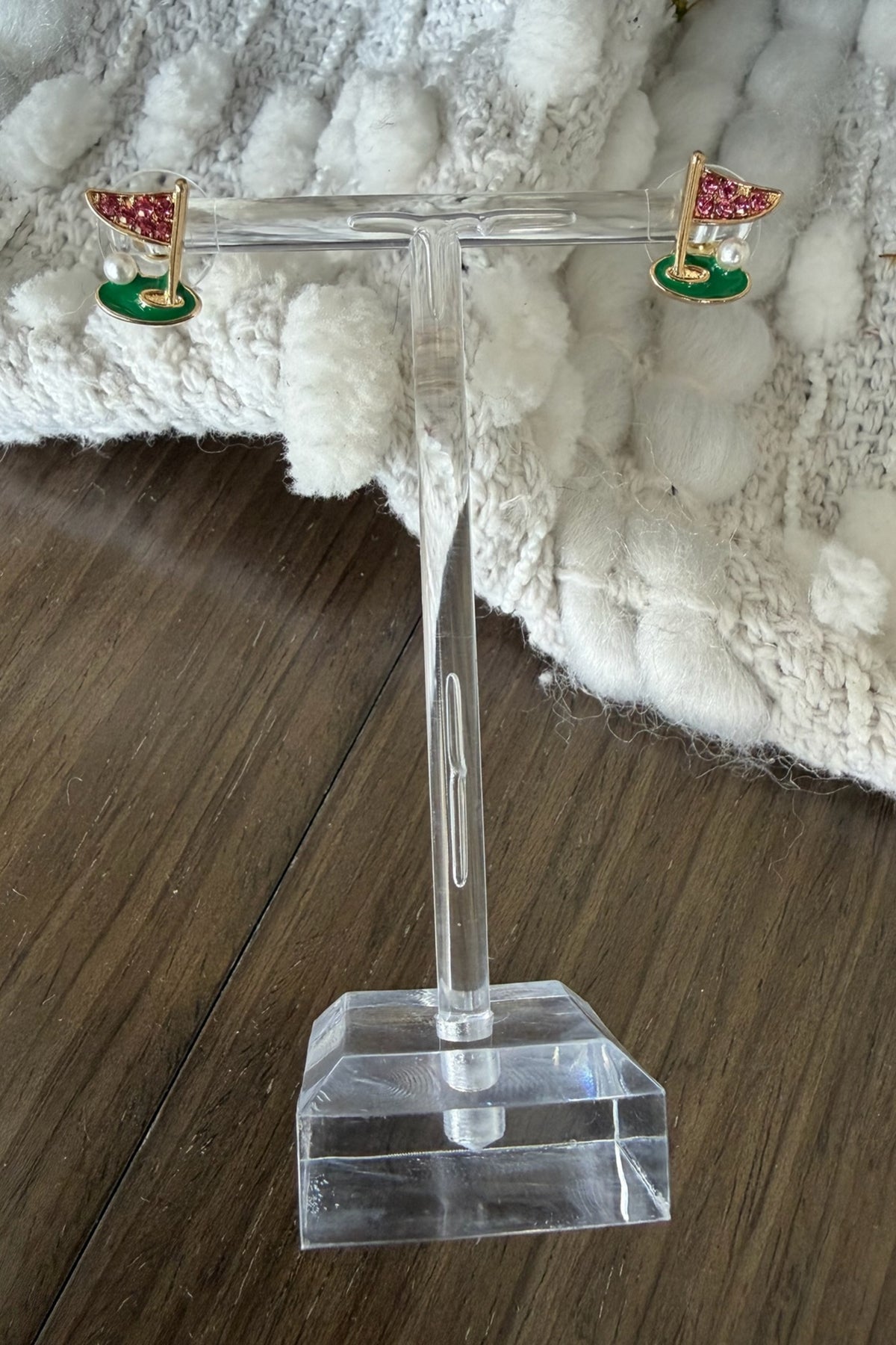 Pair of earrings on a clear stand with a textured white surface in the background