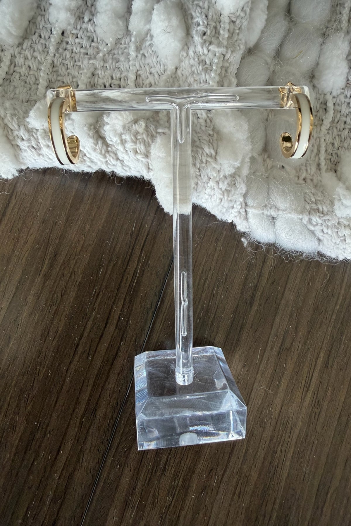Gold hoop earrings on a clear stand against a textured white and brown background