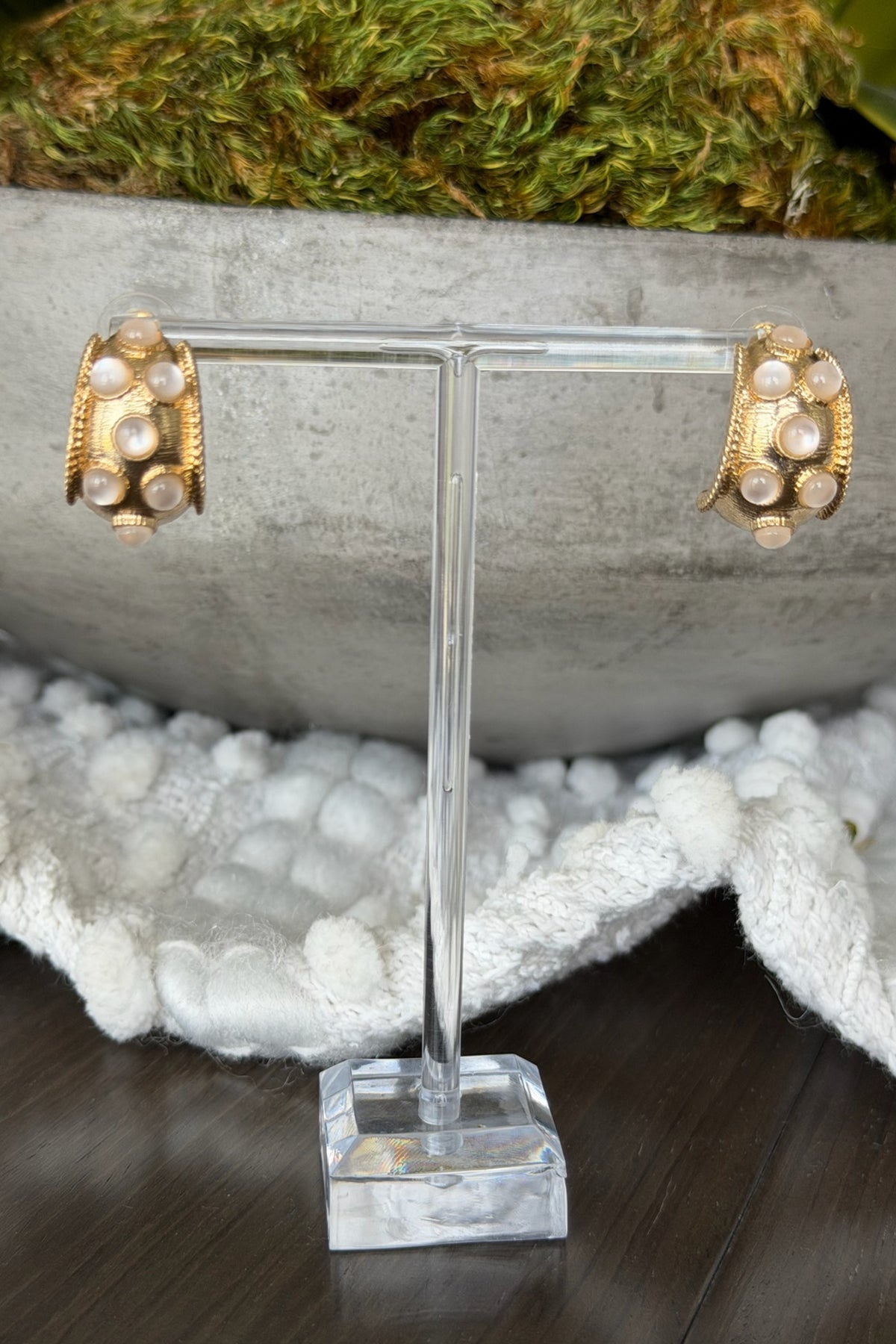 Gold earrings on a clear stand with a natural background